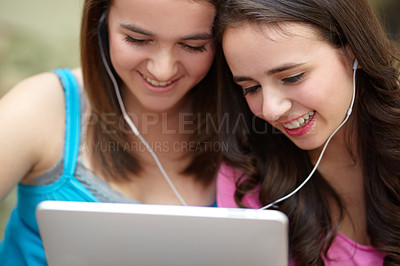 Buy stock photo Two teenage girls sharing earphones while looking a tablet