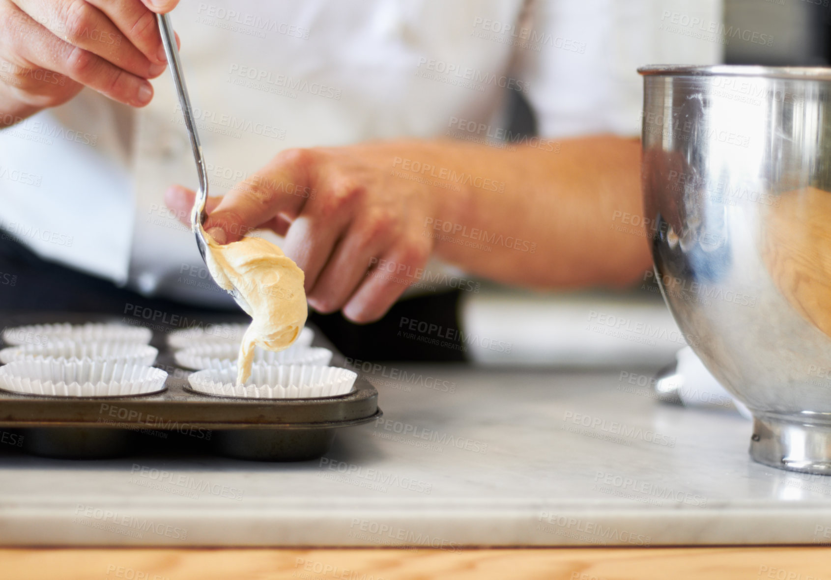 Buy stock photo A close up of a baker pushing cupcake batter from a spoon into the cupcake tray