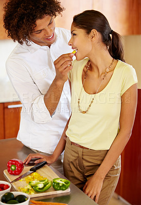 Buy stock photo A young man feeding his girlfriend a fresh pepper while cooking dinner