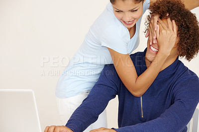 Buy stock photo Young woman covering her boyfriend&#039;s eyes while he&#039;s working on his laptop