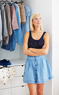 Buy stock photo Young woman standing with her arms folded in front of a wardrobe and looking contemplative