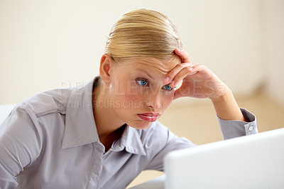 Buy stock photo An exhausted young woman looking at her laptop screen with a frown