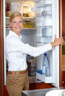 Buy stock photo A gorgeous young woman opening her fridge and smiling at you