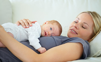 Buy stock photo Shot of a mother resting on a sofa with her newborn baby lying on her