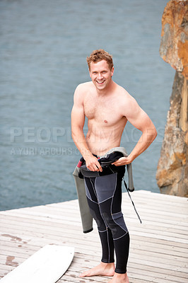 Buy stock photo Young man putting on his wetsuit before engaging in some watersports