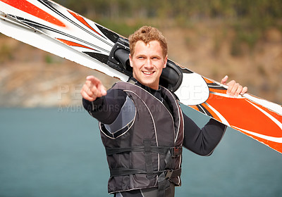Buy stock photo Smiling water-skier holding his skis alongside the lake and pointing