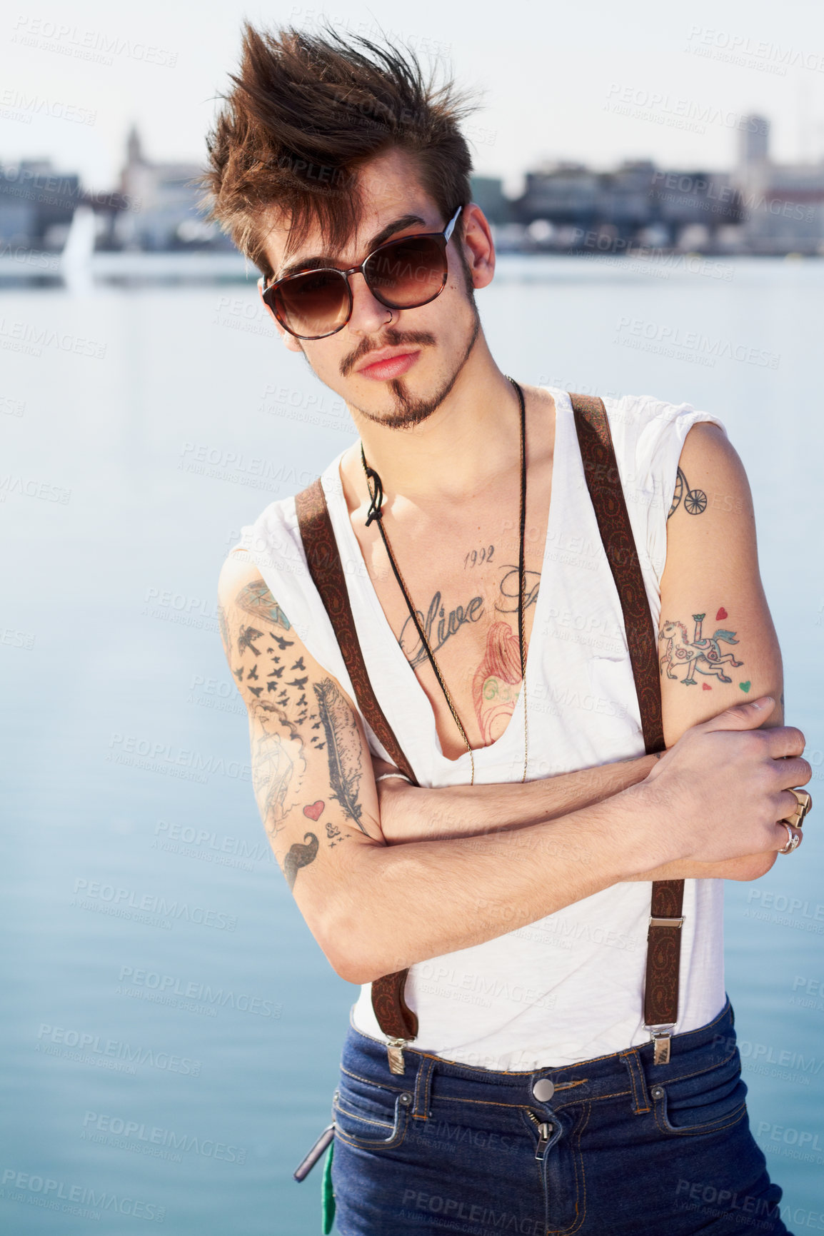 Buy stock photo Sunglasses, portrait and man by sea with arms crossed for stylish tattoo, body art and fashion. Hipster, ocean and confident male person standing outdoor in Spain with cool clothes, attitude and punk