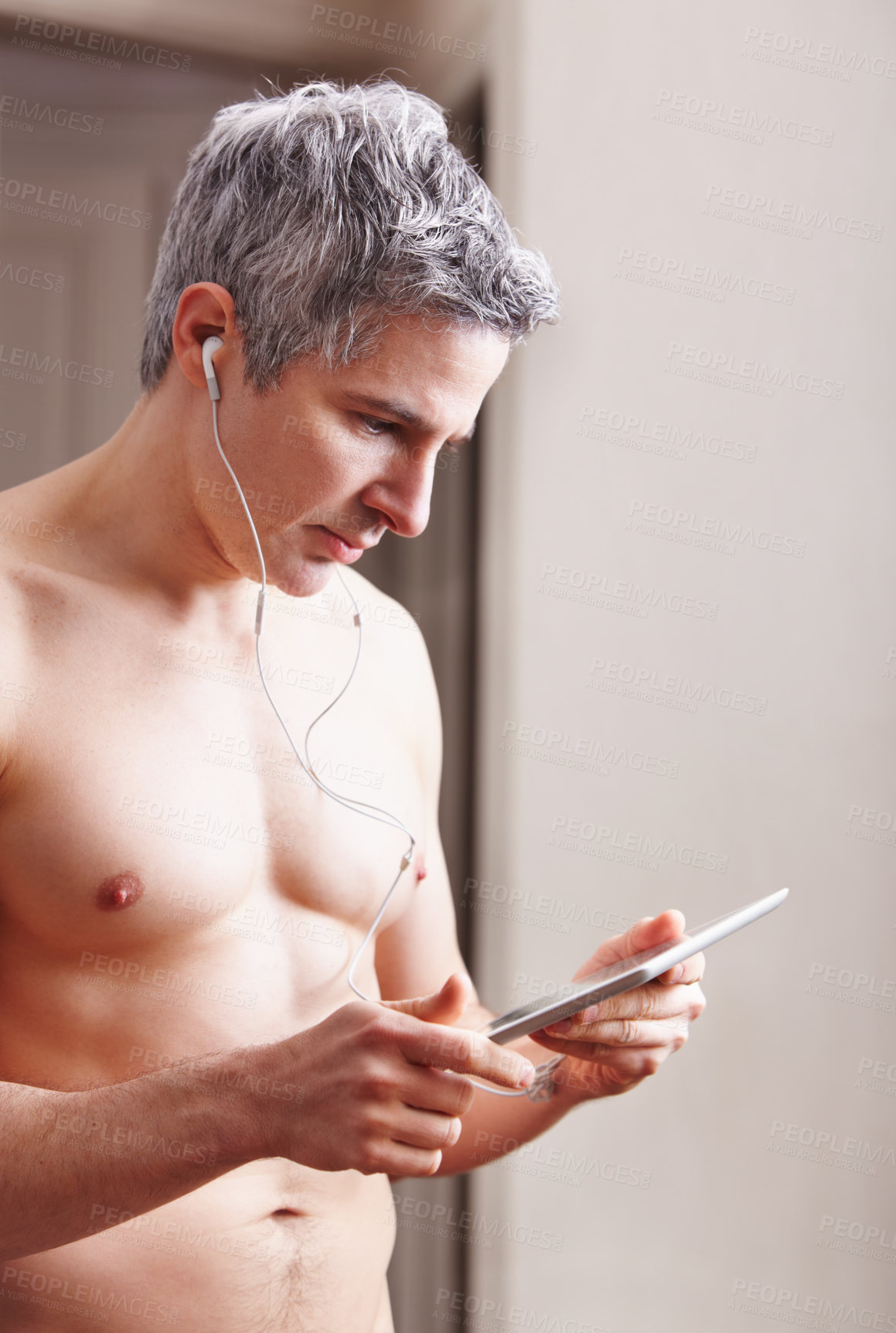 Buy stock photo A shirtless mature man wearing earphones and looking at his digital tablet