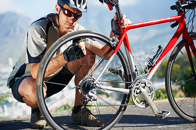 Buy stock photo Shot of a cyclist checking the wheel on his bicycle
