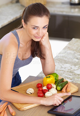 Buy stock photo An attractive young woman looking for recipes on her digital tablet while cooking