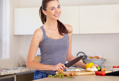 Buy stock photo An attractive young woman chopping up vegetables in the kitchen