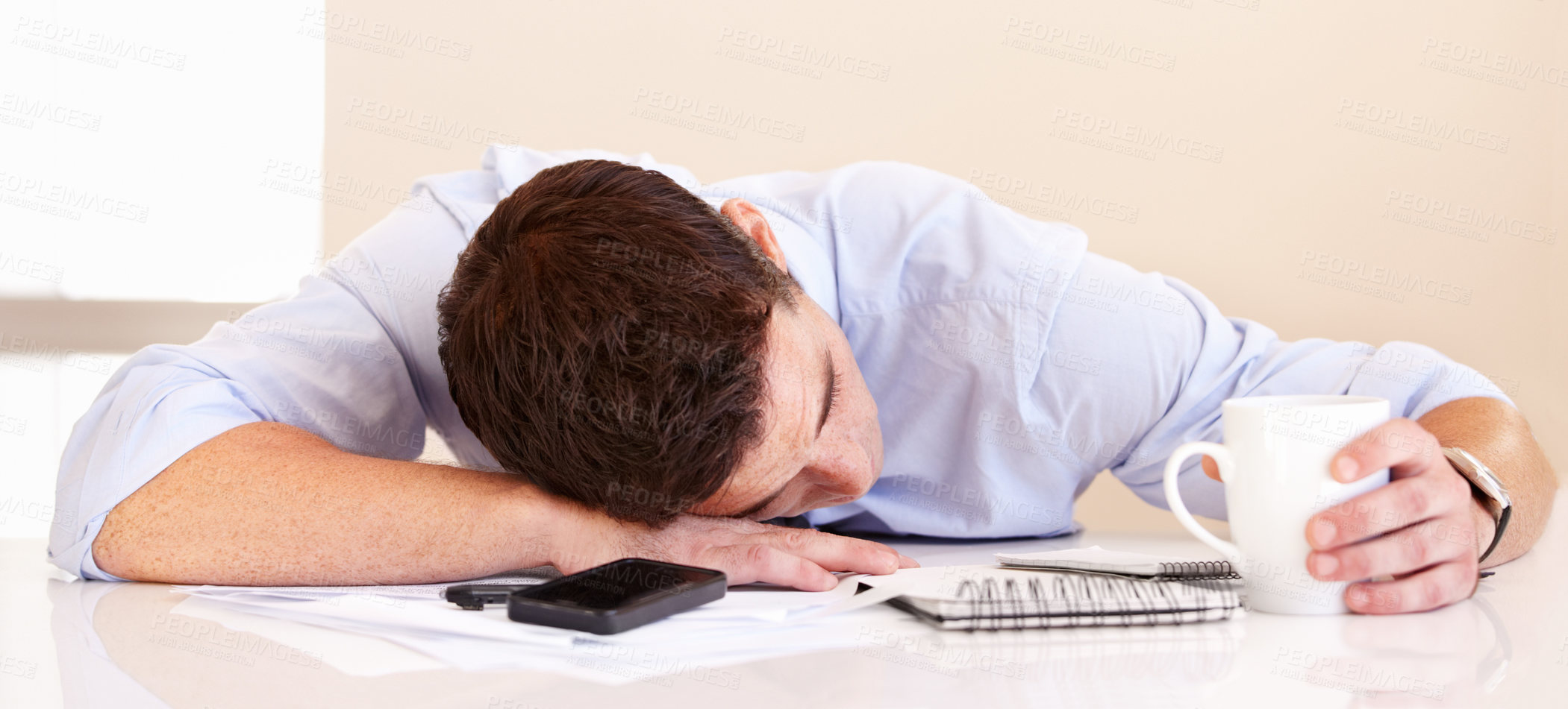 Buy stock photo Exhausted businessman lying on his desk along with his mobile phone