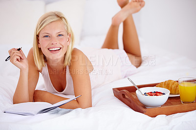 Buy stock photo Blonde woman lying on her bed and writing in her diary with her breakfast next to her
