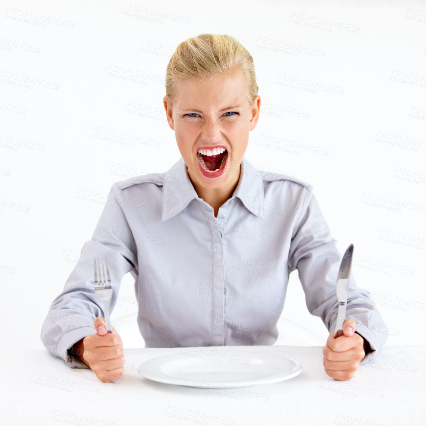 Buy stock photo Furious young woman sitting in front of an empty plate while holding her knife and fork
