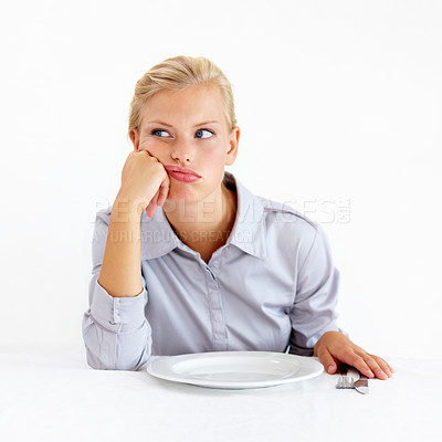 Buy stock photo Bored young woman sitting in front of an empty plate looking pissed off