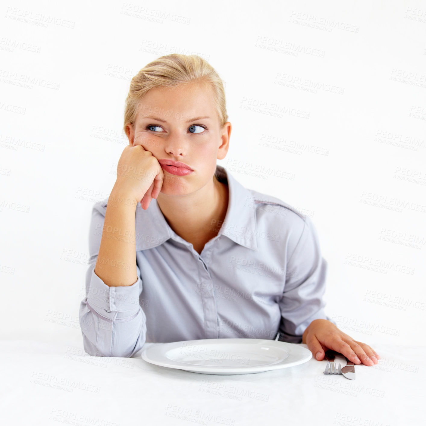 Buy stock photo Bored young woman sitting in front of an empty plate looking pissed off