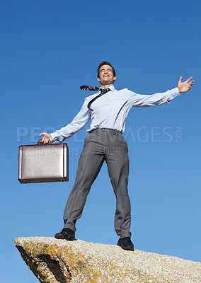 Buy stock photo An elated young businessman holding a briefcase standing atop a cliff