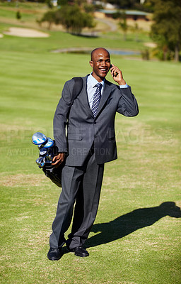 Buy stock photo Shot of an african wearing a suit and talking on the phone while carrying a golf bag on a golf course