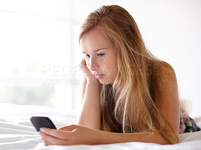 Buy stock photo Shot of a beautiful young woman reading a text message while lying on her bed