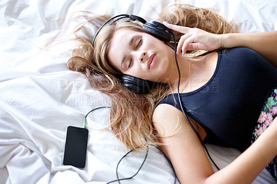Buy stock photo Shot of a beautiful young woman listening to music while relaxing on her bed
