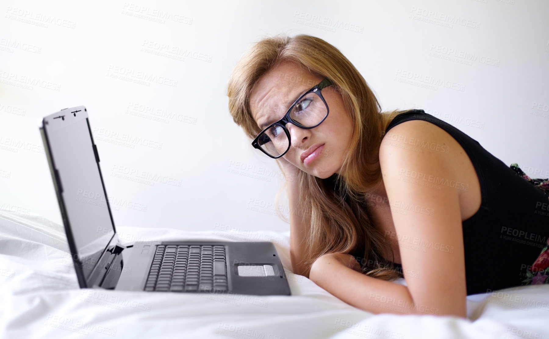 Buy stock photo Shot of a beautiful young woman looking unsure while using a laptop on her bed