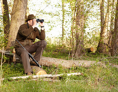 Buy stock photo A game ranger looking through his binoculars while sitting on a log