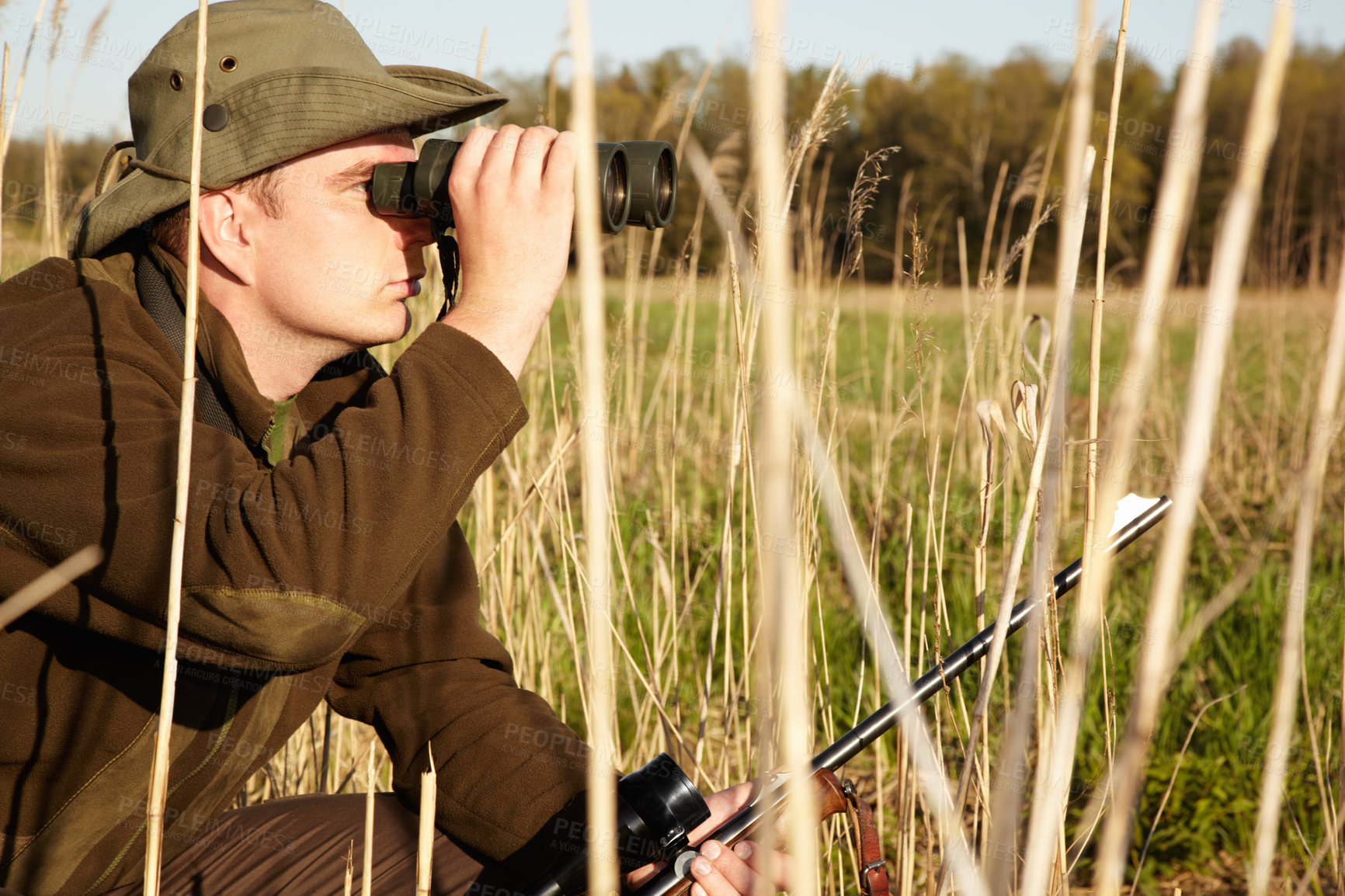 Buy stock photo A man in the wildlife looking through his binoculars holding his rifle