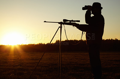 Buy stock photo A silhouette of a man in the wildlife with his sniper rifle ready and looking through his binoculars