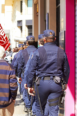 Buy stock photo Rearview shot of a line of police walking down a street on a day of protest