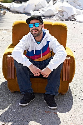 Buy stock photo A trendy male with sunglasses and a cap on smiling and sitting on a couch in the outdoors