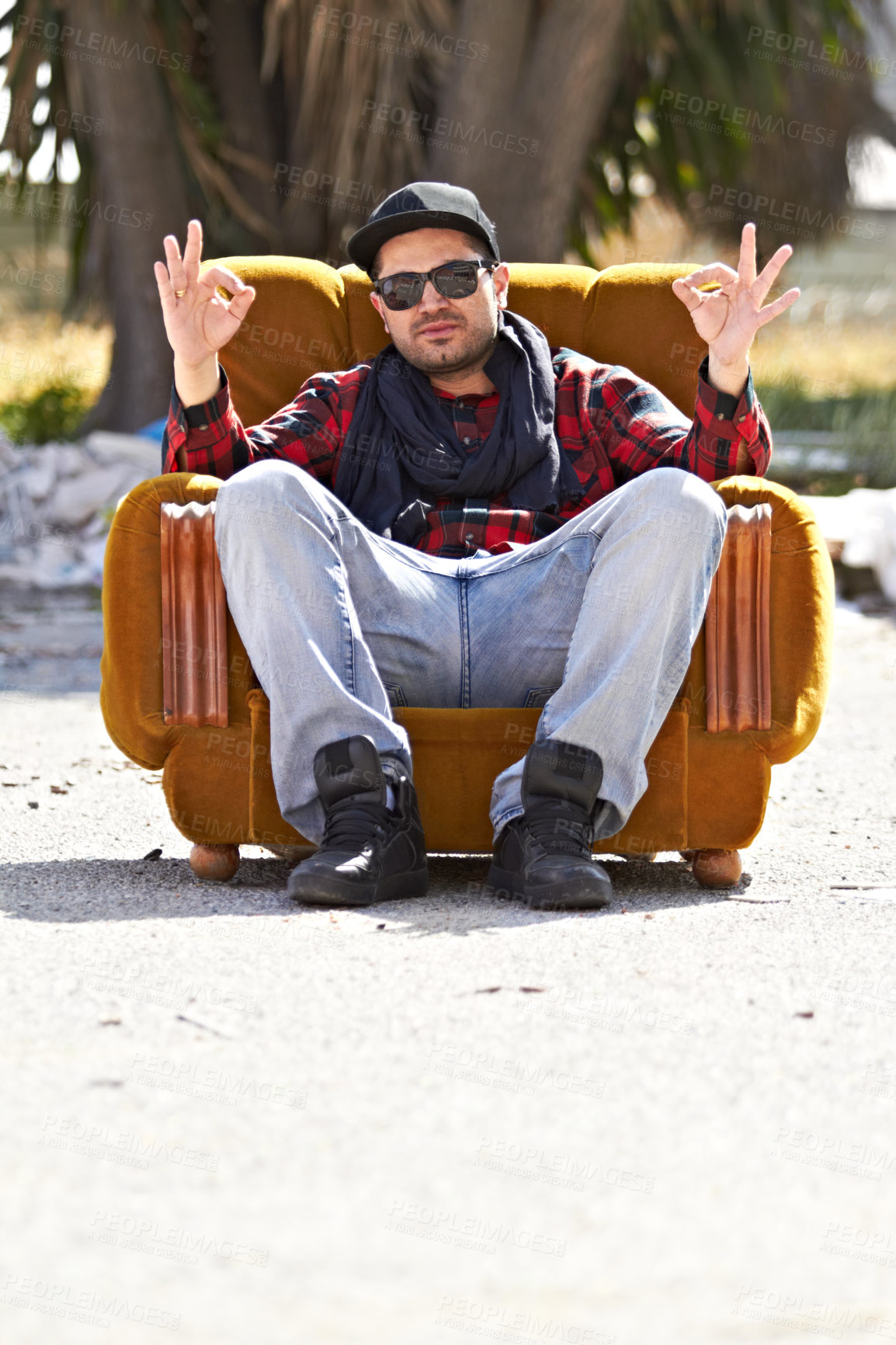 Buy stock photo A confident male sitting on a couch in the road holding up hand signs