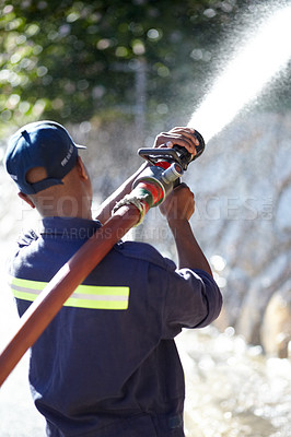 Buy stock photo Rearview shot of a fireman spraying water with a fire hose