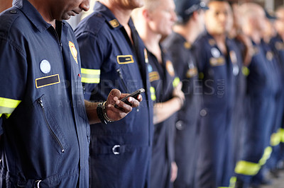 Buy stock photo A fireman using his cellphone while standing in a row with his colleagues