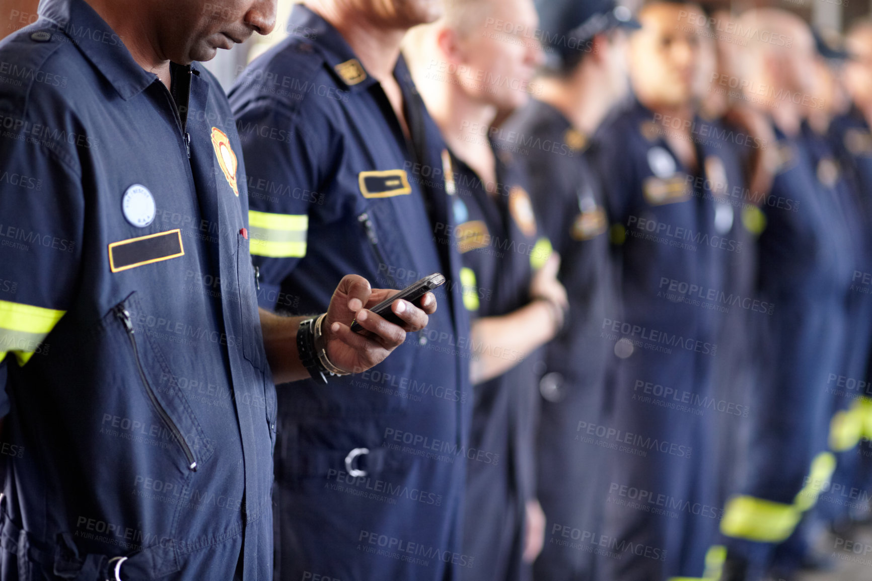 Buy stock photo A fireman using his cellphone while standing in a row with his colleagues