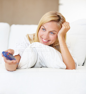 Buy stock photo An attractive young woman switching channels with the tv remote
