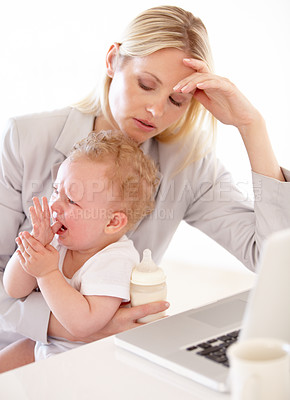 Buy stock photo An overwhelmed mom sitting in front of the computer with her crying baby