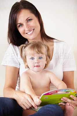 Buy stock photo A cute little girl sitting on her mother's lap with a book