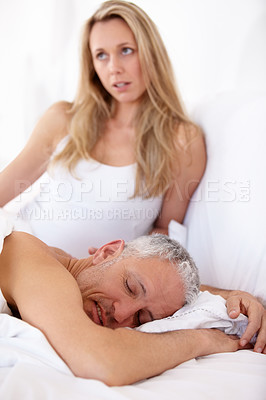 Buy stock photo A woman sitting up in bed with dissatisfied expression while her husband sleeps