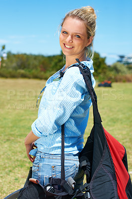 Buy stock photo Woman, portrait or smile outdoor with grass, bags and casual fashion for travel or vacation with blue sky. Person, face or tourist and happy in nature for adventure, holiday or parachute experience