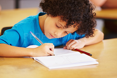 Buy stock photo Boy, writing and book in school classroom for learning, focus or development for future. Male child, pen and paper for studying, education and test for thinking, scholarship or concentration in class