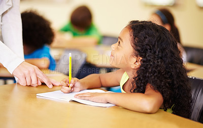 Buy stock photo School, education and kids with a student girl in a classroom, writing while talking to her teacher. Children, learning and study with an adorable female kid at a desk in class for child development
