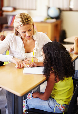 Buy stock photo Teaching, writing and teacher helping child at school with education, learning or development. Woman talking to girl student with notebook, pencil and knowledge at classroom desk with support