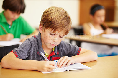 Buy stock photo Boy kid, school classroom and writing test with focus, concentration and thinking for education goals. Male child, book and pen in class for assessment, studying or learning at desk for scholarship