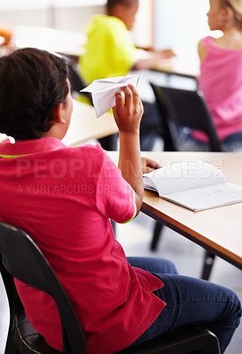 Buy stock photo Bully, boy child with paper plane in classroom and sitting at his desk with behavior problem. Naughty or bad, distracted male student in class and playing with prank in school building on chair