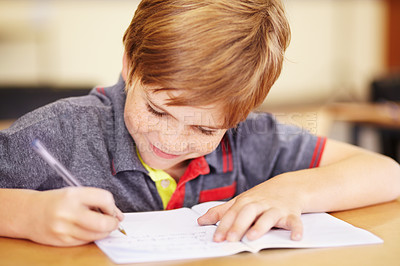 Buy stock photo A cute little boy doing his homework in class