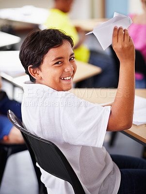 Buy stock photo Portrait, student and paper plane in classroom and happy, learning at desks or Indian boy, play and origami jet or class distraction. Playful smile, kid and holding airplane and middle school fun