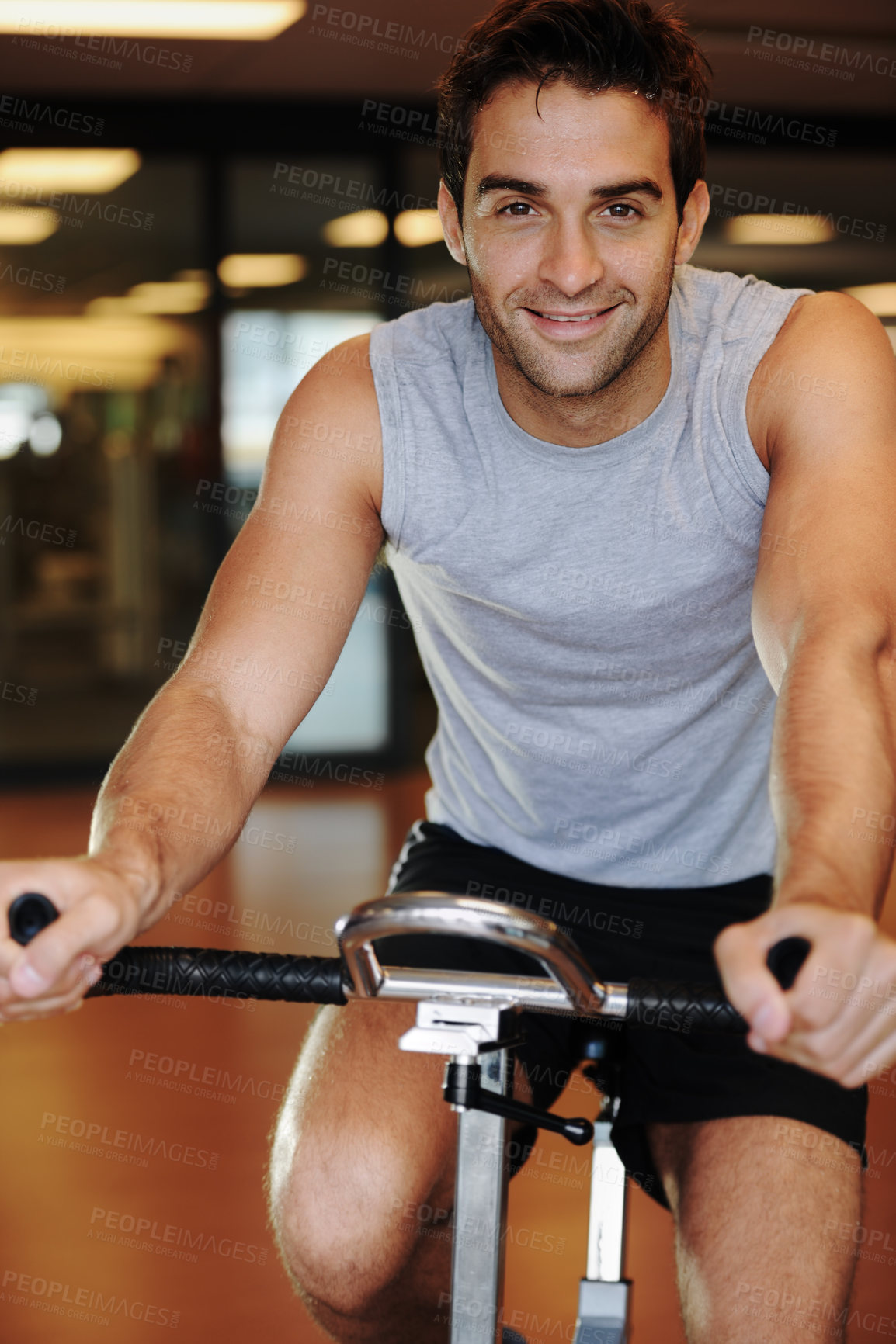 Buy stock photo A smiling handsome young man wearing sport clothing and using a exercise bike at the gym