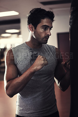 Buy stock photo Profile of a handsome man wearing sport clothing and standing ready to punch a punching bag at the gym