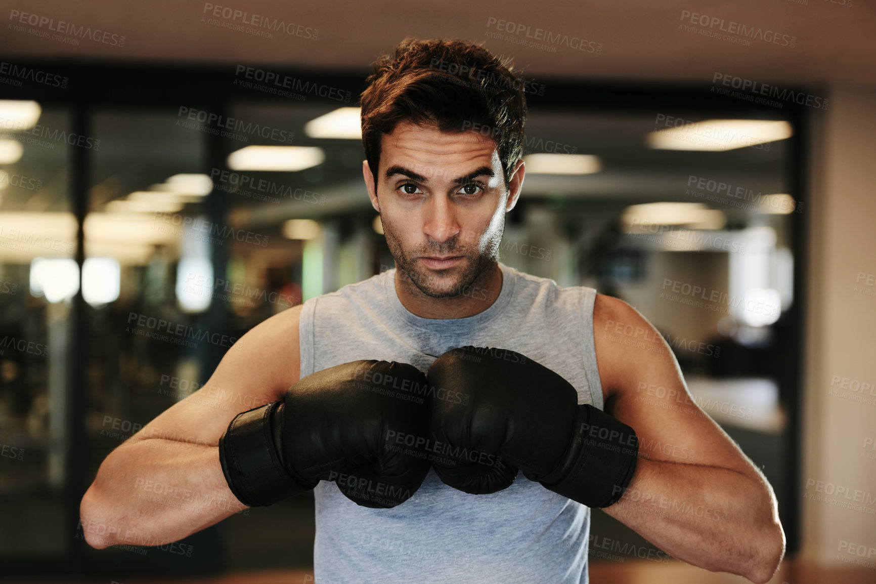 Buy stock photo Portrait of a focused man wearing boxing gloves and sport clothing posing ready to fight at the gym