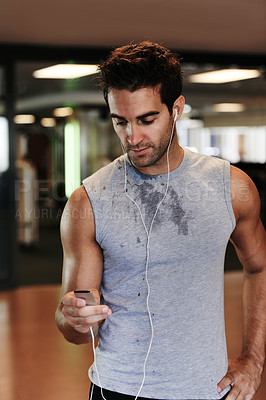 Buy stock photo A handsome man standing at the gym wearing sports clothing and using his mp3 player